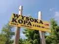 Żółta tablica na drewnianych słupach informuje: Wysoka Kopa, Góry Izerskie, 1126 m n.p.m. To szczyt Korony Gór Polski.