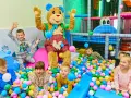 Klimczok z dzieckiem w basenie pełnym kolorowych piłeczek. Radosne dzieci bawią się z pluszowym misiem.