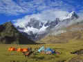 Obóz pod majestatyczną Cordillera Blanca. Namioty, ludzie i muły na zielonej łące, w tle ośnieżone szczyty.