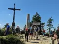 Grupa turystów na szczycie Turbacz z Koninek. Widoczny krzyż, pomnik i drewniana wiata.