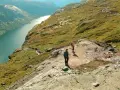 Dwie osoby wędrują po skalistym szlaku w górach Norwegii, podziwiając malowniczy fiord.