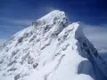 Ośnieżony, skalisty szczyt Mount Everest, z kilkoma wspinaczami na grani. Widać ślady na śniegu, jak wygląda szczyt Mount Everest.