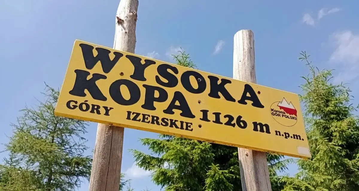 Żółta tablica na drewnianych słupach informuje: Wysoka Kopa, Góry Izerskie, 1126 m n.p.m. To szczyt Korony Gór Polski.