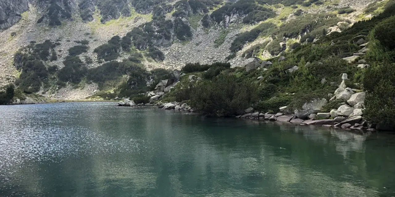 Spokojne jezioro odbija skaliste zbocza gór Pirin porośnięte kosodrzewiną.
