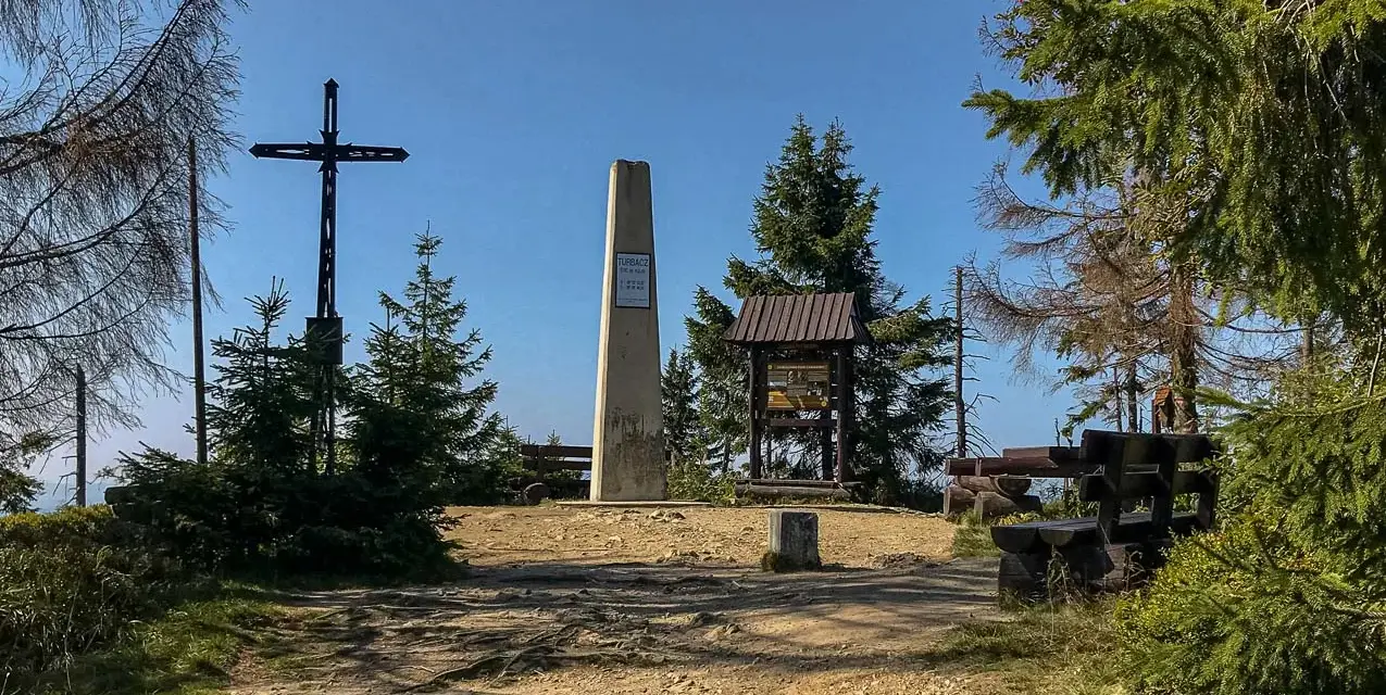 Na szczycie Turbacz, wśród **gorących szczytów**, stoi krzyż i obelisk. Wokół ławki i tablice informacyjne.