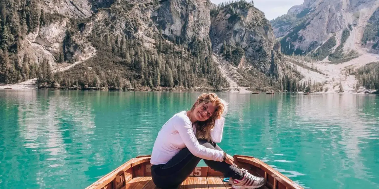 Kobieta w łodzi na turkusowym jeziorze w Dolomitach, w tle góry.