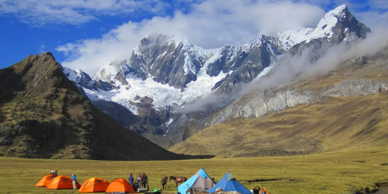 Obóz pod majestatyczną Cordillera Blanca. Namioty, ludzie i muły na zielonej łące, w tle ośnieżone szczyty.