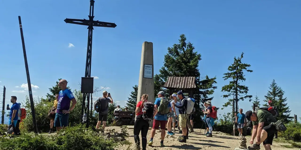 Grupa turystów na szczycie Turbacz z Koninek. Widoczny krzyż, pomnik i drewniana wiata.
