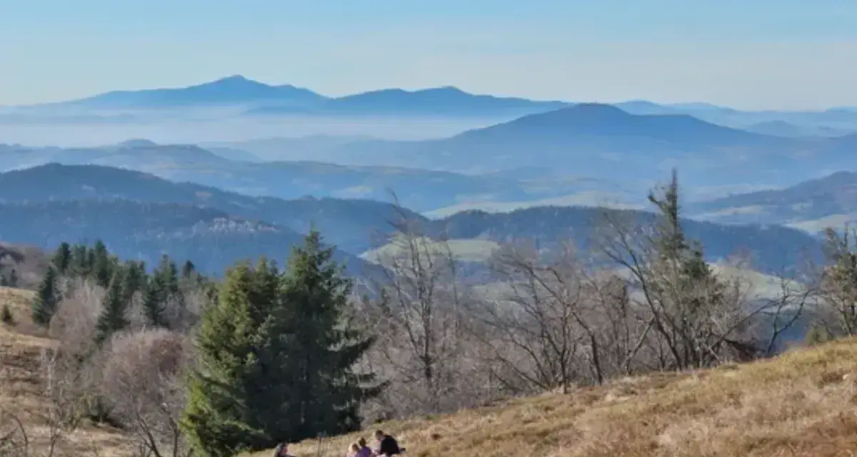 Widok na Beskid Wyspowy z malowniczymi miejscowościami w oddali. Ludzie odpoczywają na zboczu góry.