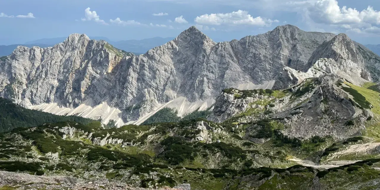 Majestatyczne, skaliste szczyty górskie Triglav z zielonymi zboczami i chmurami na niebie.
