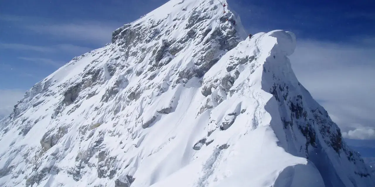 Ośnieżony, skalisty szczyt Mount Everest, z kilkoma wspinaczami na grani. Widać ślady na śniegu, jak wygląda szczyt Mount Everest.