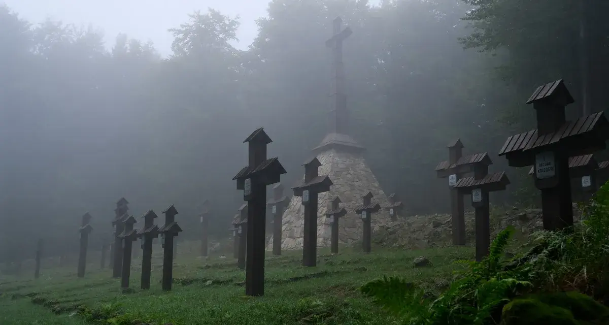 Mglisty cmentarz wojenny na Magurze Małastowskiej. Drewniane krzyże wznoszą się wśród drzew, tworząc przejmujący widok.