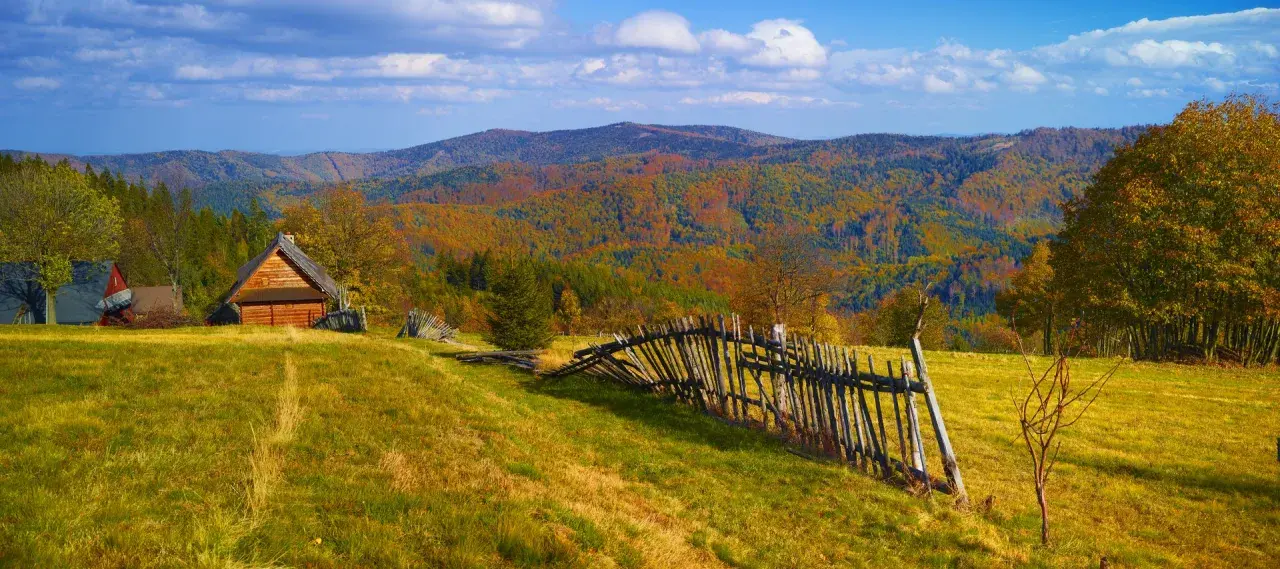 Jesienny krajobraz górski z drewnianym domkiem i potrójną palisadą.
