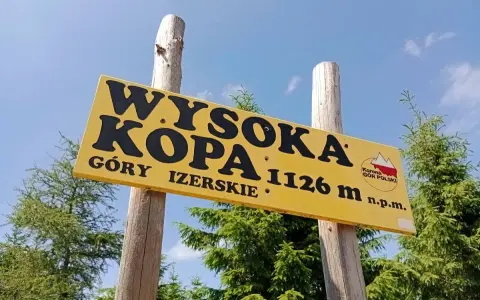 Żółta tablica na drewnianych słupach informuje: Wysoka Kopa, Góry Izerskie, 1126 m n.p.m. To szczyt Korony Gór Polski.