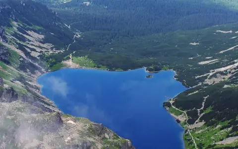 Górski staw gąsienicowy otoczony zielonymi zboczami i lasem iglastym.