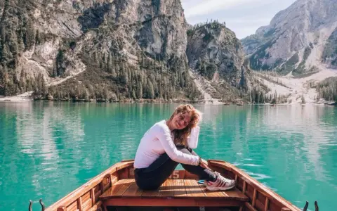 Kobieta w łodzi na turkusowym jeziorze w Dolomitach, w tle góry.