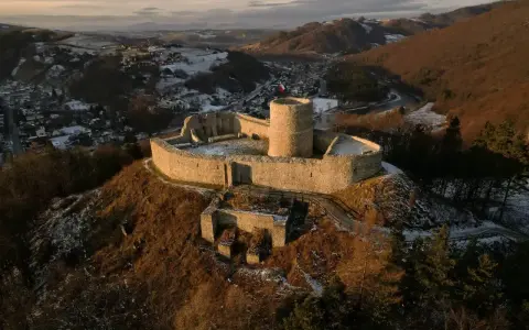 Ruiny zamku na wzgórzu, z widokiem na dolinę i miasteczko, w zimowej scenerii.