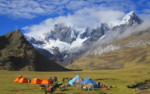 Obóz pod majestatyczną Cordillera Blanca. Namioty, ludzie i muły na zielonej łące, w tle ośnieżone szczyty.