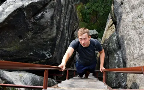 Młody mężczyzna wspina się po drewnianych schodach w skalnym mieście. Sprawdź aktualny skalne miasto cennik, by zaplanować swoją przygodę!