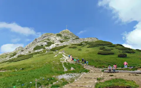 Tłum turystów wspina się kamienistym szlakiem na Giewont. Widać krzyż na szczycie.