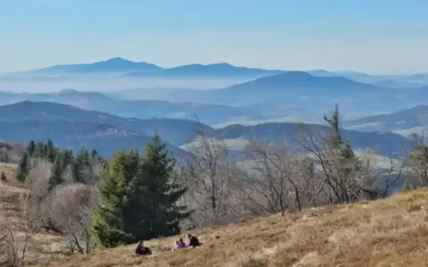 Widok na Beskid Wyspowy z malowniczymi miejscowościami w oddali. Ludzie odpoczywają na zboczu góry.