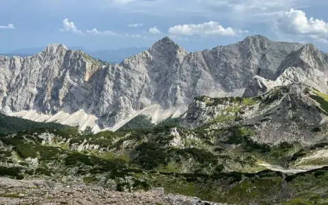 Majestatyczne, skaliste szczyty górskie Triglav z zielonymi zboczami i chmurami na niebie.