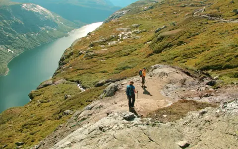 Dwie osoby wędrują po skalistym szlaku w górach Norwegii, podziwiając malowniczy fiord.