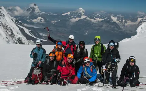 Grupa alpinistów na tle majestatycznego Monte Rosa, gotowa do zdobycia szczytu.