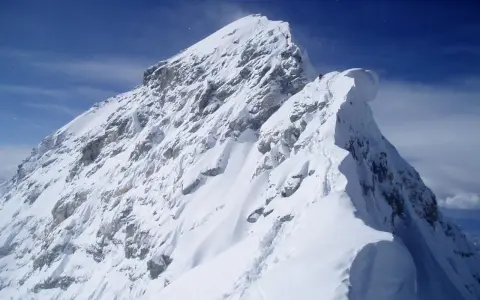 Ośnieżony, skalisty szczyt Mount Everest, z kilkoma wspinaczami na grani. Widać ślady na śniegu, jak wygląda szczyt Mount Everest.