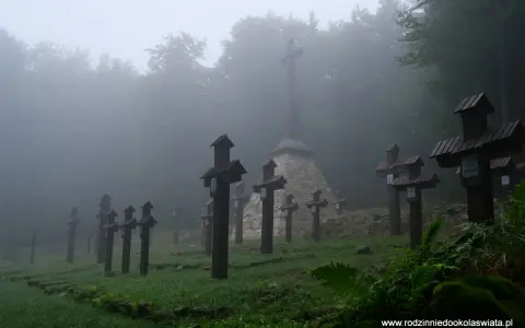 Mglisty cmentarz wojenny na Magurze Małastowskiej. Drewniane krzyże wznoszą się wśród drzew, tworząc przejmujący widok.