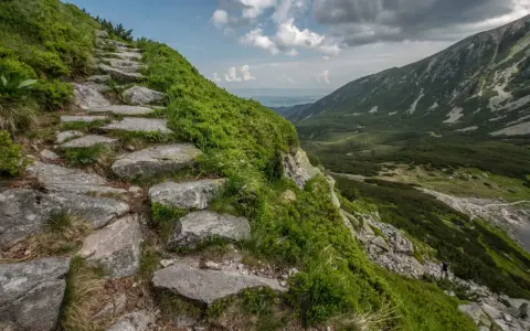 Kamieniste schody wiodące na szlak na Kościelec, otoczone zielenią kosodrzewiny. W oddali widać dolinę i góry.