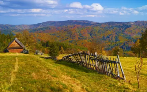 Jesienny krajobraz górski z drewnianym domkiem i potrójną palisadą.