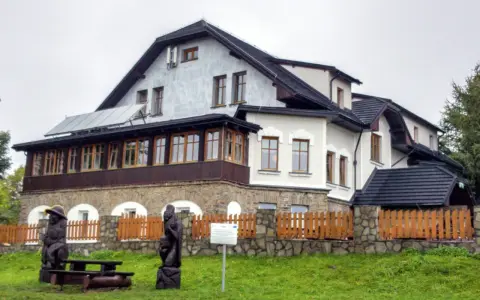 Drewniane rzeźby i ławka przed pensjonatem, idealne miejsce na odpoczynek po wędrówce po **Magurka szlaki**.