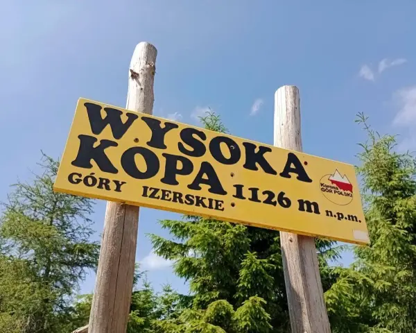 Żółta tablica na drewnianych słupach informuje: Wysoka Kopa, Góry Izerskie, 1126 m n.p.m. To szczyt Korony Gór Polski.
