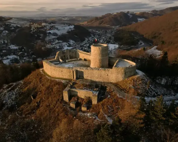 Ruiny zamku na wzgórzu, z widokiem na dolinę i miasteczko, w zimowej scenerii.
