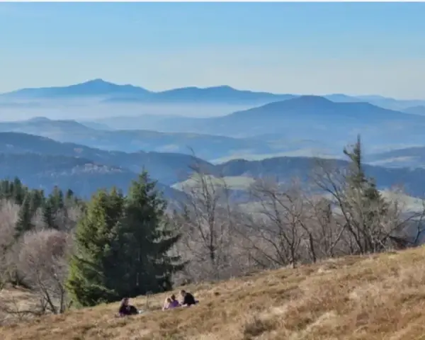 Widok na Beskid Wyspowy z malowniczymi miejscowościami w oddali. Ludzie odpoczywają na zboczu góry.