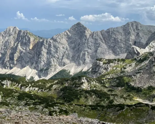 Majestatyczne, skaliste szczyty górskie Triglav z zielonymi zboczami i chmurami na niebie.