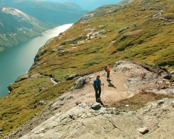 Dwie osoby wędrują po skalistym szlaku w górach Norwegii, podziwiając malowniczy fiord.