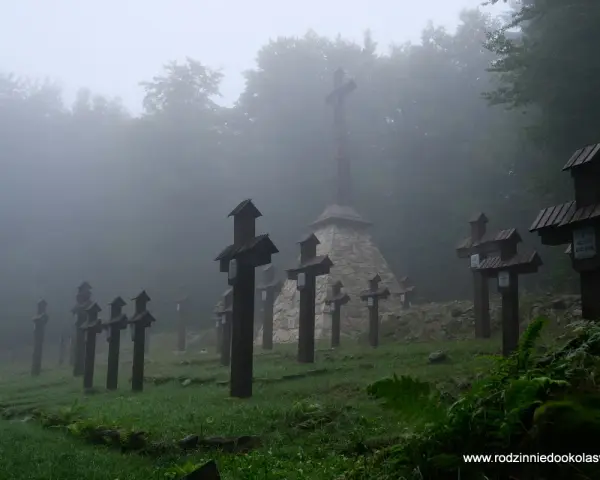 Mglisty cmentarz wojenny na Magurze Małastowskiej. Drewniane krzyże wznoszą się wśród drzew, tworząc przejmujący widok.
