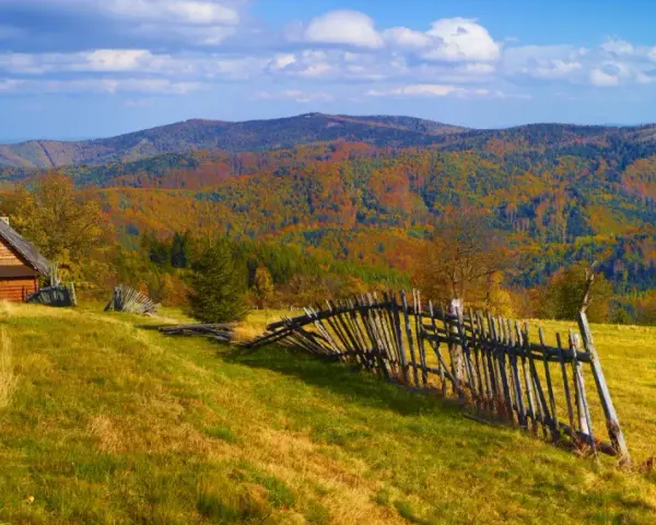 Jesienny krajobraz górski z drewnianym domkiem i potrójną palisadą.