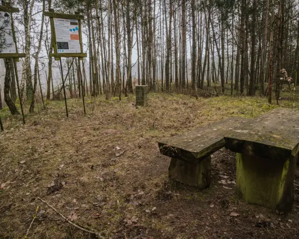 Kamienna ława i stoły w lesie, obok tablice informacyjne. Miejsce idealne na odpoczynek podczas wędrówki po górach obkaskich.