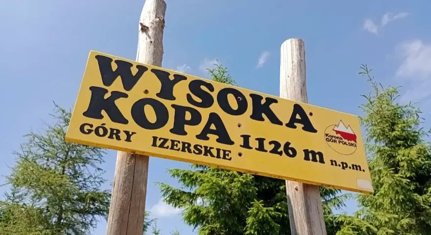 Żółta tablica na drewnianych słupach informuje: Wysoka Kopa, Góry Izerskie, 1126 m n.p.m. To szczyt Korony Gór Polski.