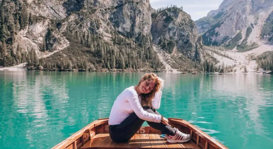 Kobieta w łodzi na turkusowym jeziorze w Dolomitach, w tle góry.