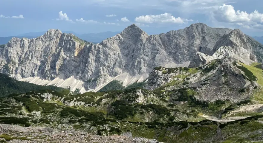 Majestatyczne, skaliste szczyty górskie Triglav z zielonymi zboczami i chmurami na niebie.