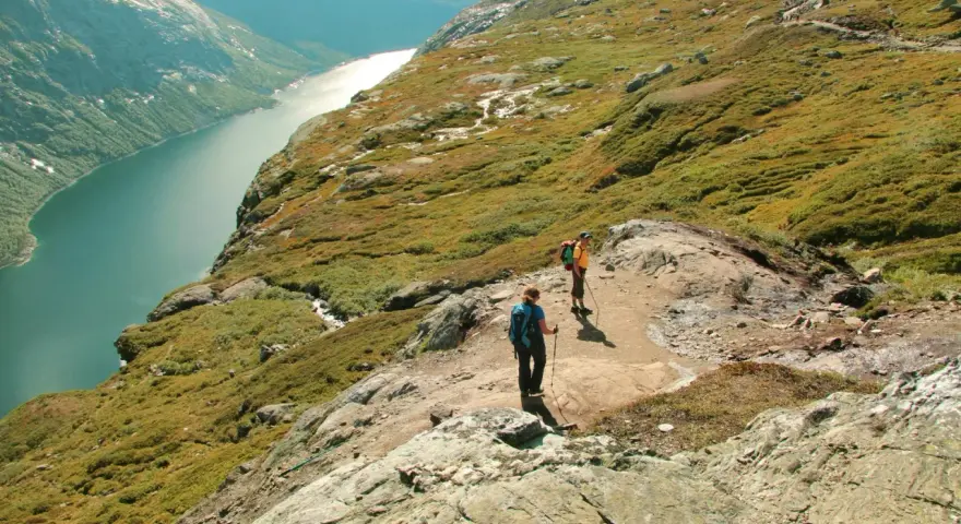 Dwie osoby wędrują po skalistym szlaku w górach Norwegii, podziwiając malowniczy fiord.