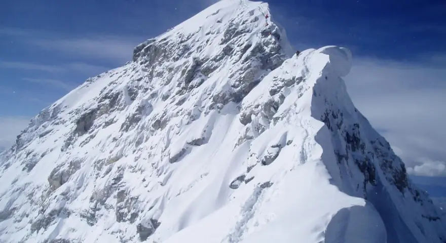 Ośnieżony, skalisty szczyt Mount Everest, z kilkoma wspinaczami na grani. Widać ślady na śniegu, jak wygląda szczyt Mount Everest.