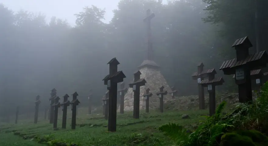 Mglisty cmentarz wojenny na Magurze Małastowskiej. Drewniane krzyże wznoszą się wśród drzew, tworząc przejmujący widok.