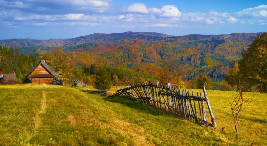 Jesienny krajobraz górski z drewnianym domkiem i potrójną palisadą.