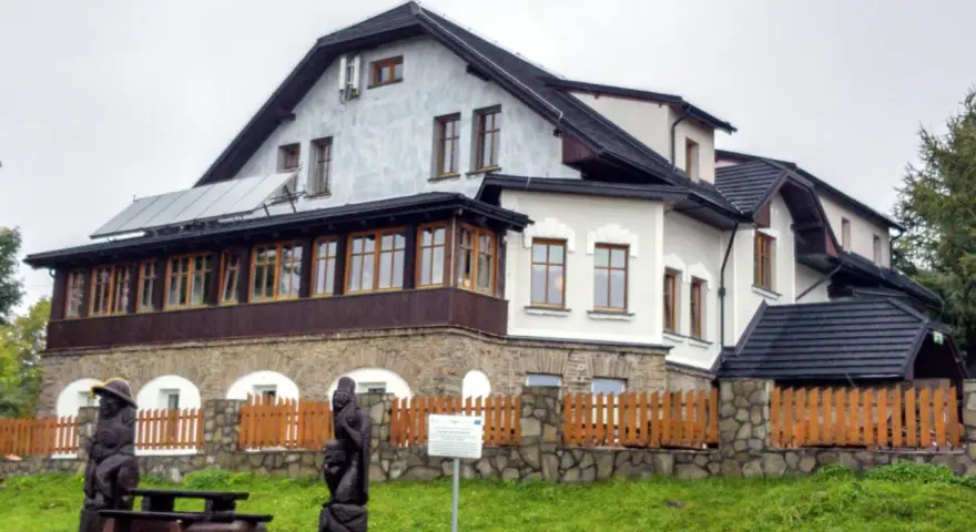 Drewniane rzeźby i ławka przed pensjonatem, idealne miejsce na odpoczynek po wędrówce po **Magurka szlaki**.