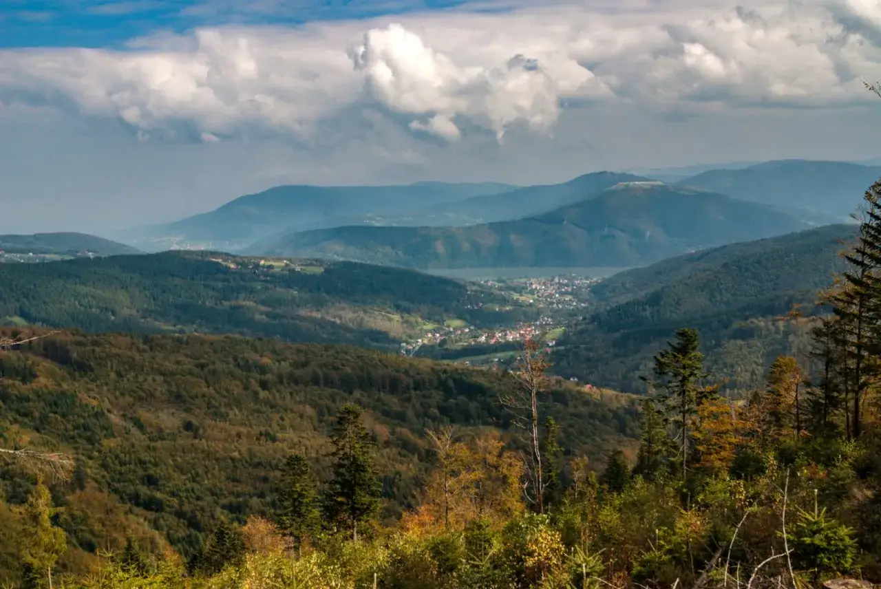 Widok z góry na dolinę z miasteczkiem, lasami i jeziorami. W oddali widać kolejne pasma górskie. Idealne miejsce na wędrówkę po Magurka szlaki.